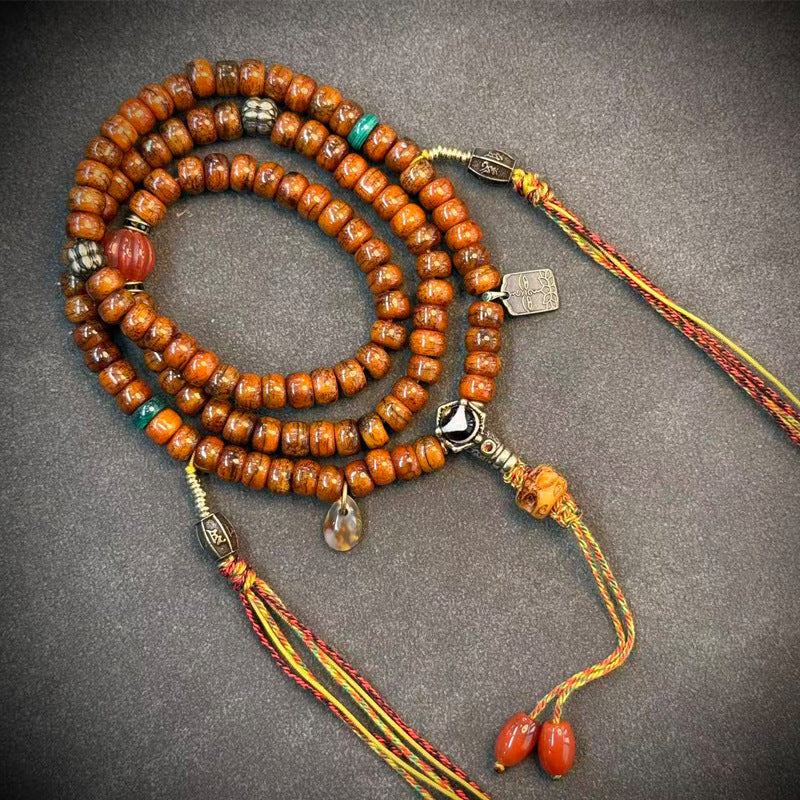 Yak bone mala coiled on grey surface with red agate, turquoise spacers and colorful ethnic tassel