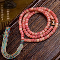 Tibetan half-red yak bone 108 mala coiled on dark wood surface with dzi stone accent and colorful tassel
