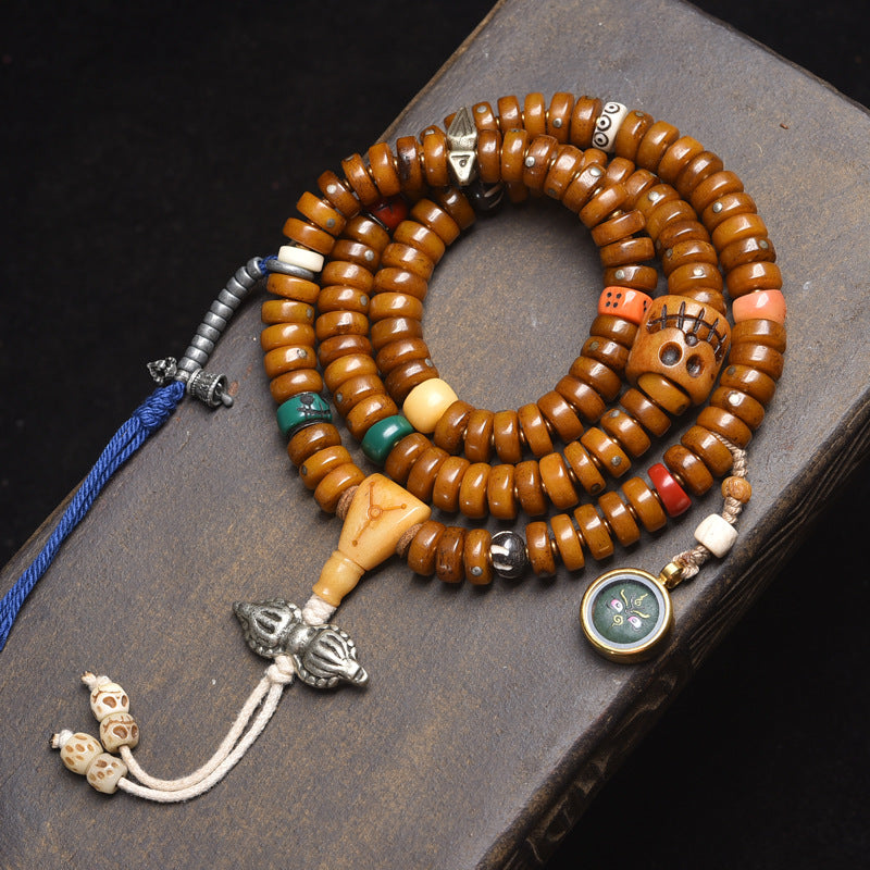 Tibetan antique recycled bone disc 108 mala coiled on dark book with skull charm, gau box and blue tassel
