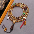 Golden turtle shell 108 mala coiled on grey surface showing full layout with all charms