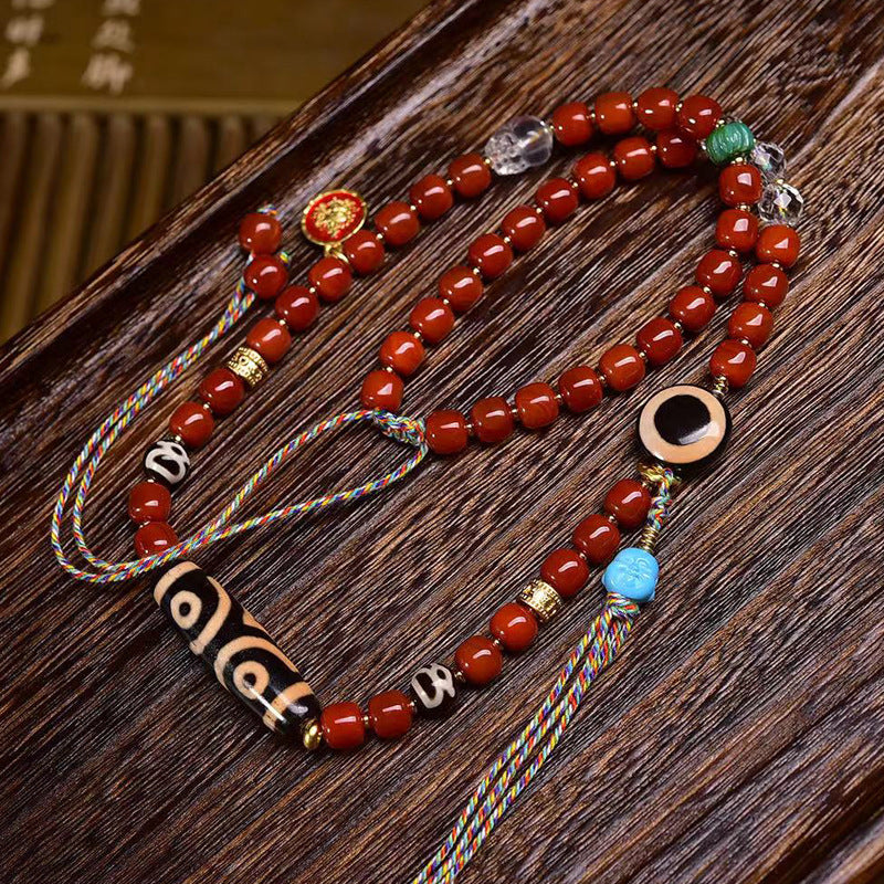 Tibetan three-eye dzi bead with red agate barrel beads and gold fittings, close-up macro shot on grey surface