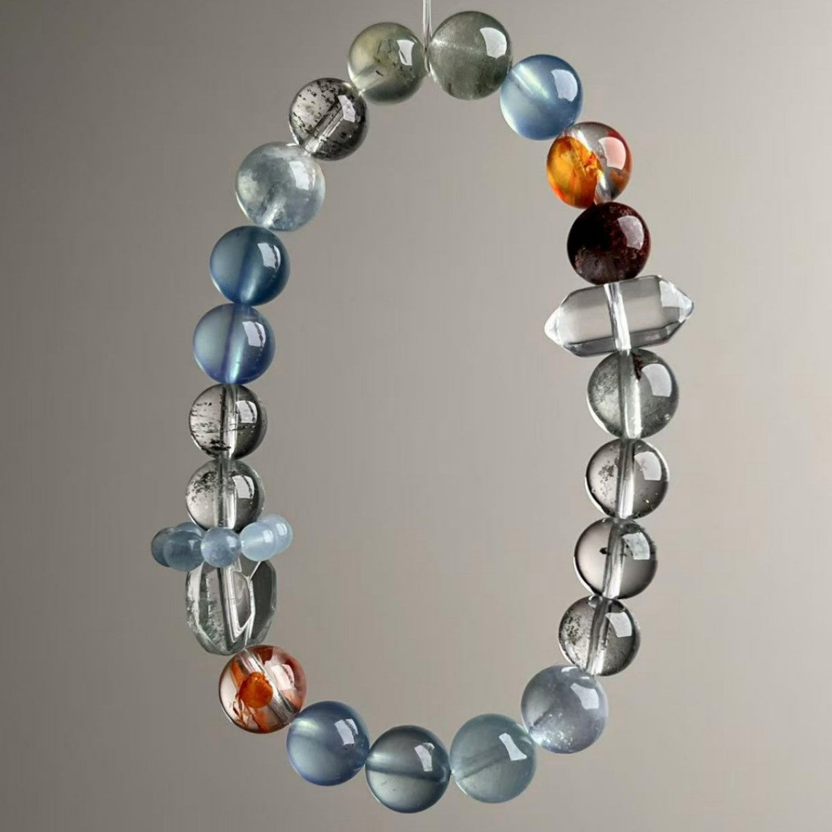 Brazilian mixed crystal bracelet with 9.5mm aquamarine, green phantom, red flower and clear quartz beads held in hand