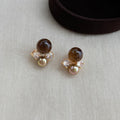 Tiger's eye and pearl stud earrings on grey knit fabric