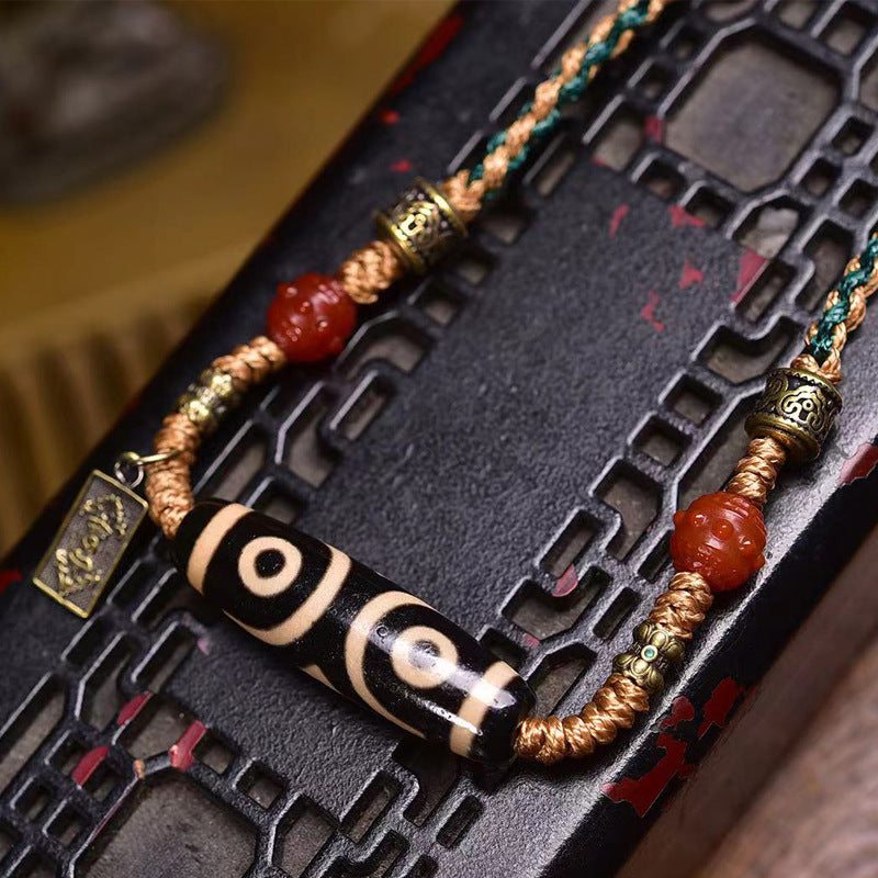 Close-up of three-eye dzi bead and two-eye dzi bead side by side on dark lattice surface with red agate and bronze metal accents