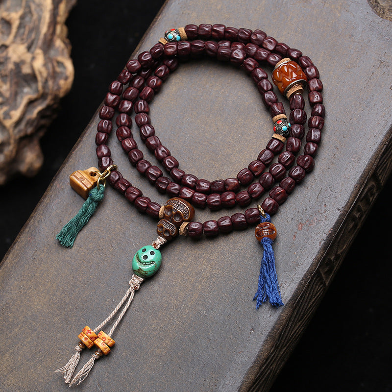 Vintage red sandalwood 108 mala laid flat on stone surface with skull guru bead and colorful tassels
