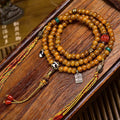 Vintage yak bone disc 108 mala coiled on dark wood tray showing full layout with all charms and tassels
