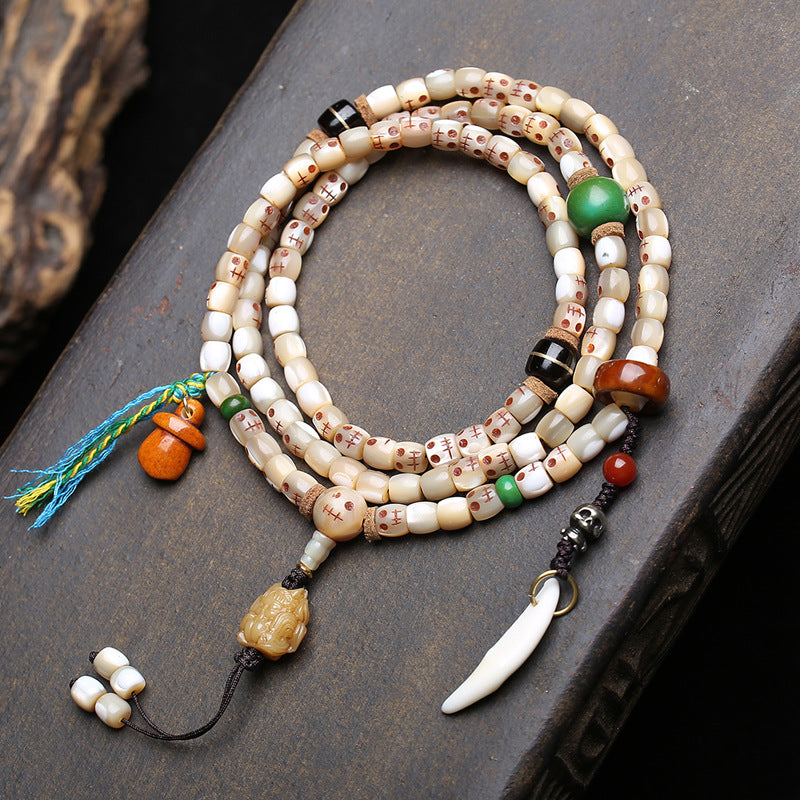 Tibetan fish bone Ah-Dai 108 mala coiled on dark stone surface showing skull beads, coconut spacers and colorful tassel