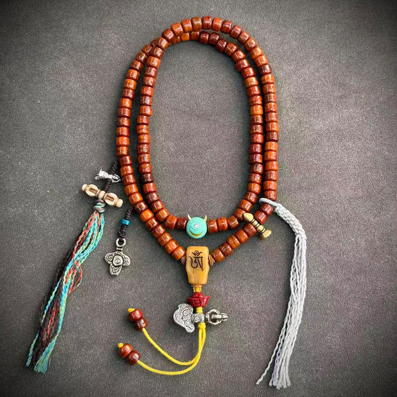 Yak bone mala coiled on grey surface with dzi bead, skull charm, silver pendant and yellow tassel