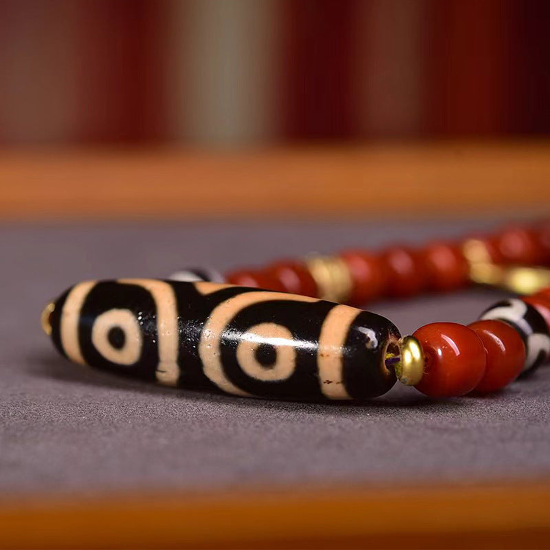 Vertical close-up of striped dzi bead with single eye motif, surrounded by red agate and gold spacer beads