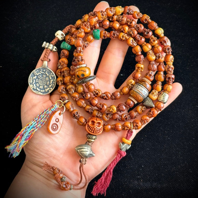 Yak bone skull mala draped over hand showing charms and tassels