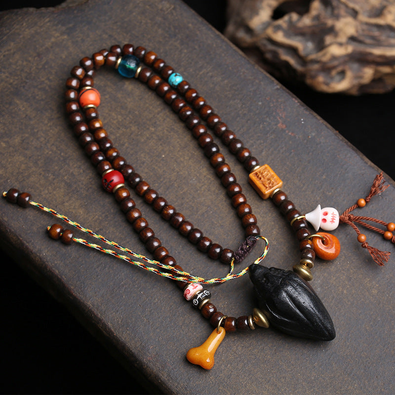 Overhead flat lay of Tibetan mala necklace on dark stone showing complete bead strand with colorful accent beads, tassels and black Tsa Tsa pendant