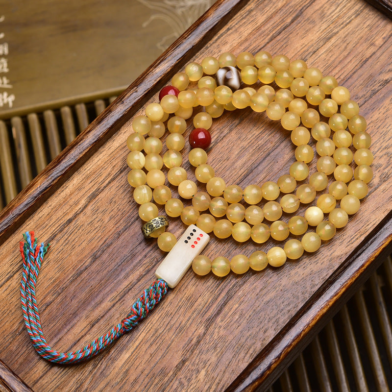 Antler mala coiled on wooden tray showing bone dice counter, red agate spacer and colorful tassel