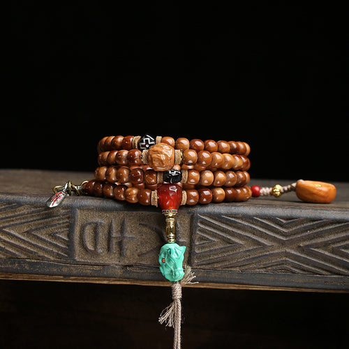 Cocos mala wrapped as multi-loop bracelet on wooden tray with turquoise horse head and red agate charm