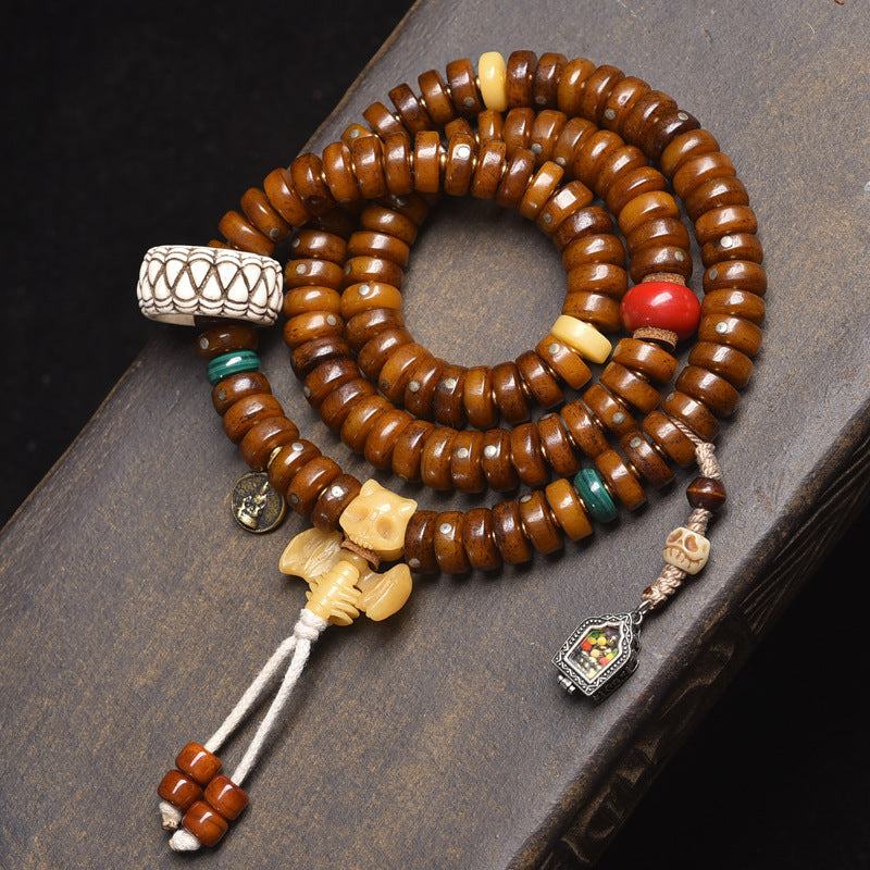 Recycled bone disc mala on dark book showing carved bone guru bead, silver coin charm and white tassel