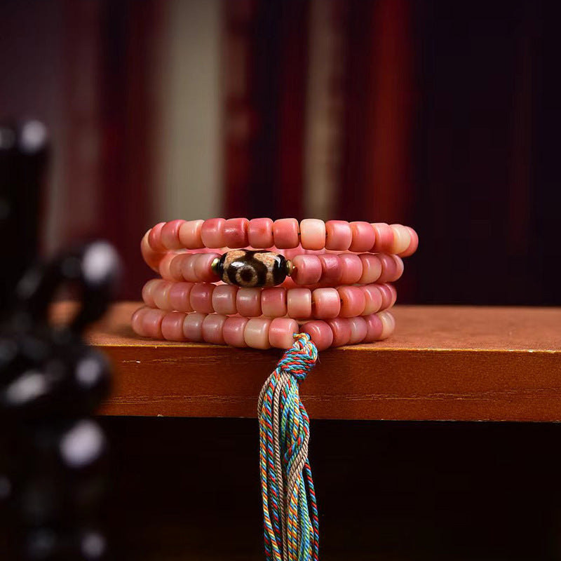Half-red yak bone mala wrapped as multi-loop bracelet on wooden ledge showing dzi bead and colorful tassel
