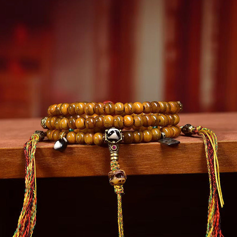 Yak bone mala wrapped as multi-loop bracelet on wooden edge showing dzi bead and colorful tassels