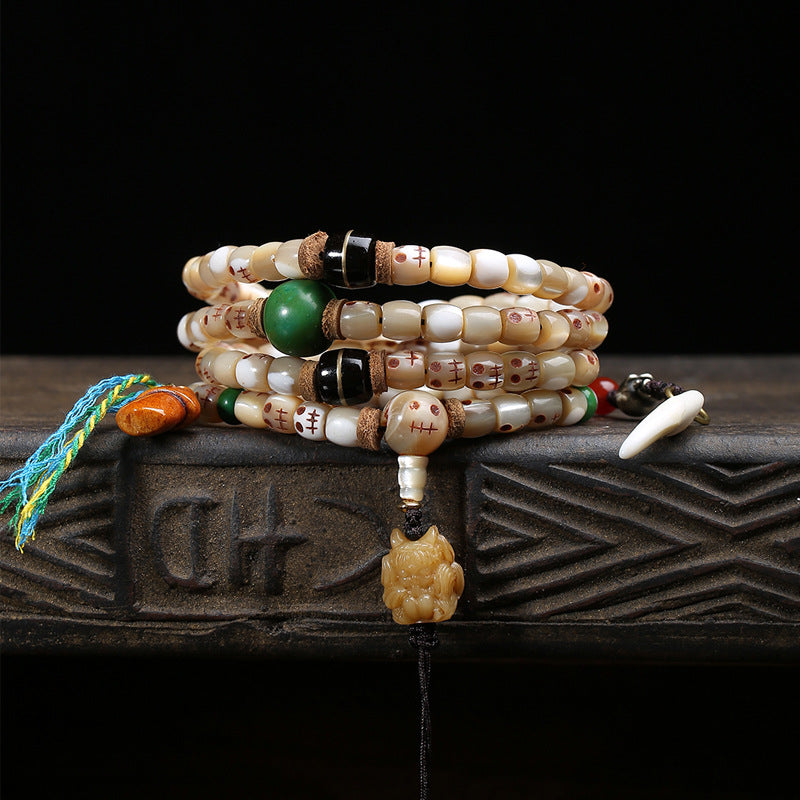 Fish bone Ah-Dai mala wrapped as multi-loop bracelet on dark wooden box showing green jade bead and dzi stone