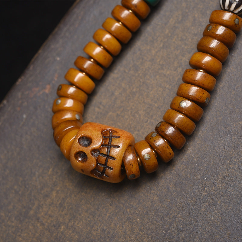 Close-up of hand-carved skull charm on recycled bone disc mala showing warm honey patina