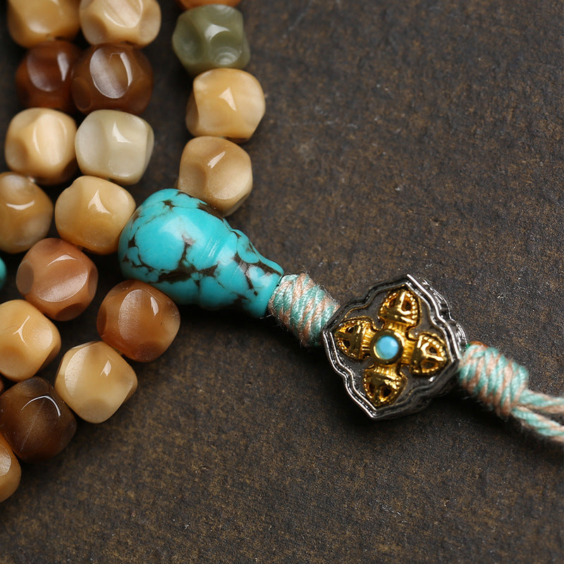 Close-up of turquoise guru bead and copper vajra ornament with linen tassel on dragon spine mala