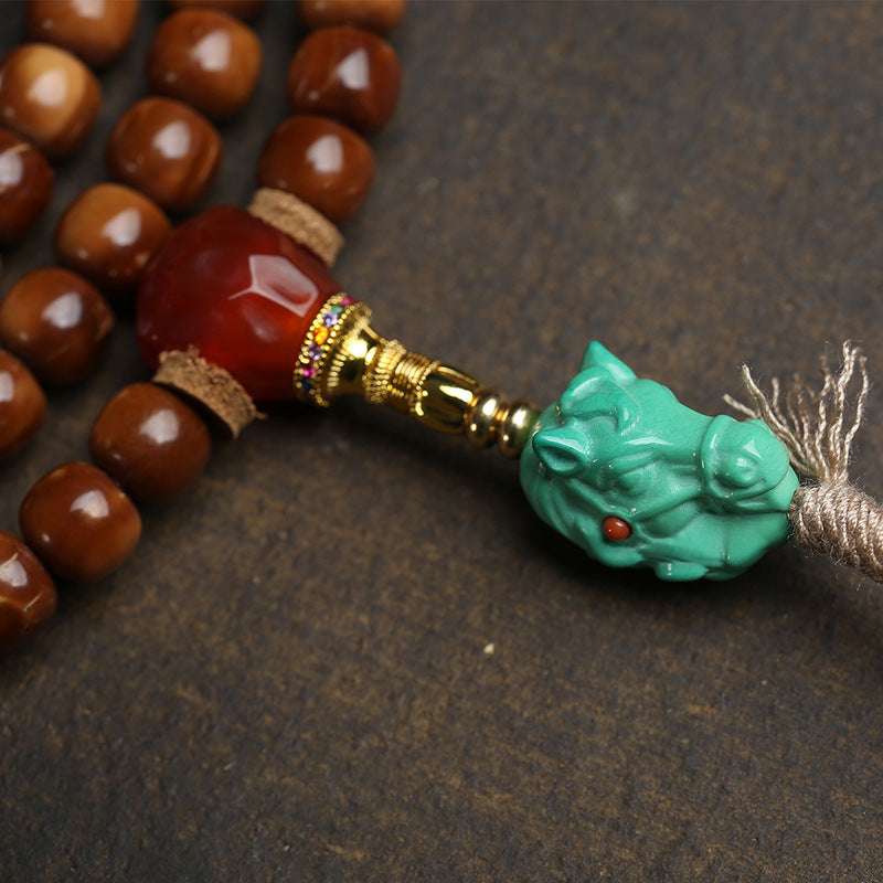 Close-up of red agate guru bead and turquoise horse head pendant with gold connector on cocos mala
