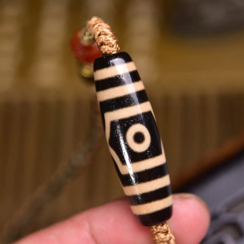 Hand holding single-eye dzi bead close-up showing black and white striped vintage pattern texture on woven cord