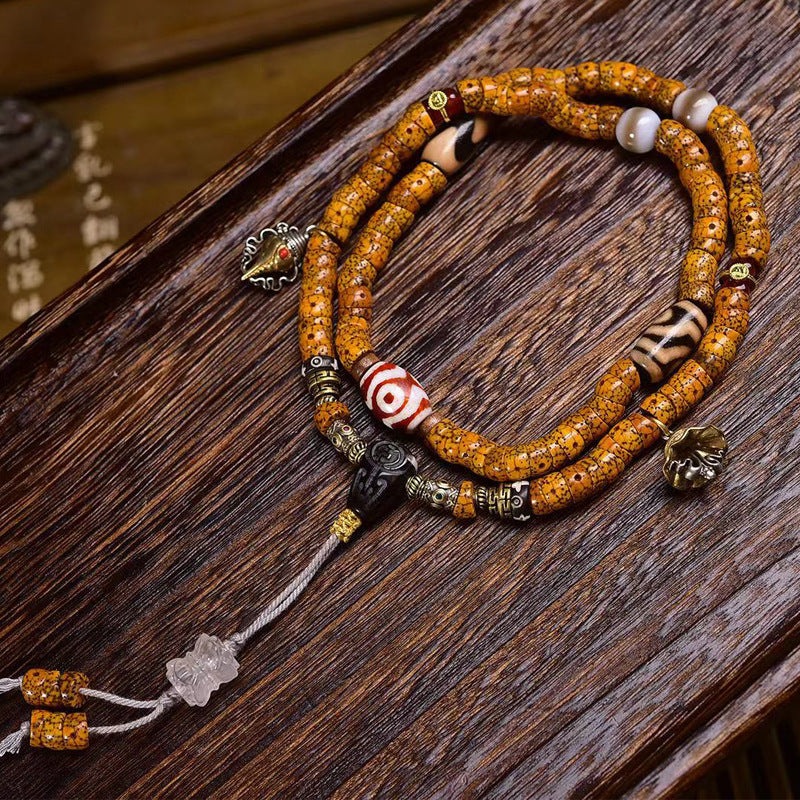 Close-up of crescent star bodhi mala on dark wood showing dzi bead, agate and conch pendant