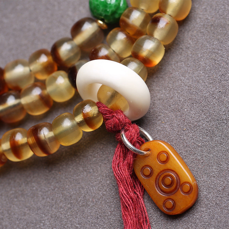 Detail of bone ring, red tassel and carved dzi pendant on turtle shell mala