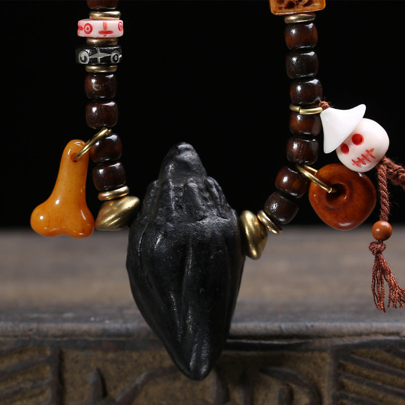Close-up detail of hand-carved black Nala Tsa Tsa amulet pendant with amber gourd charm and white skull ornament against dark background