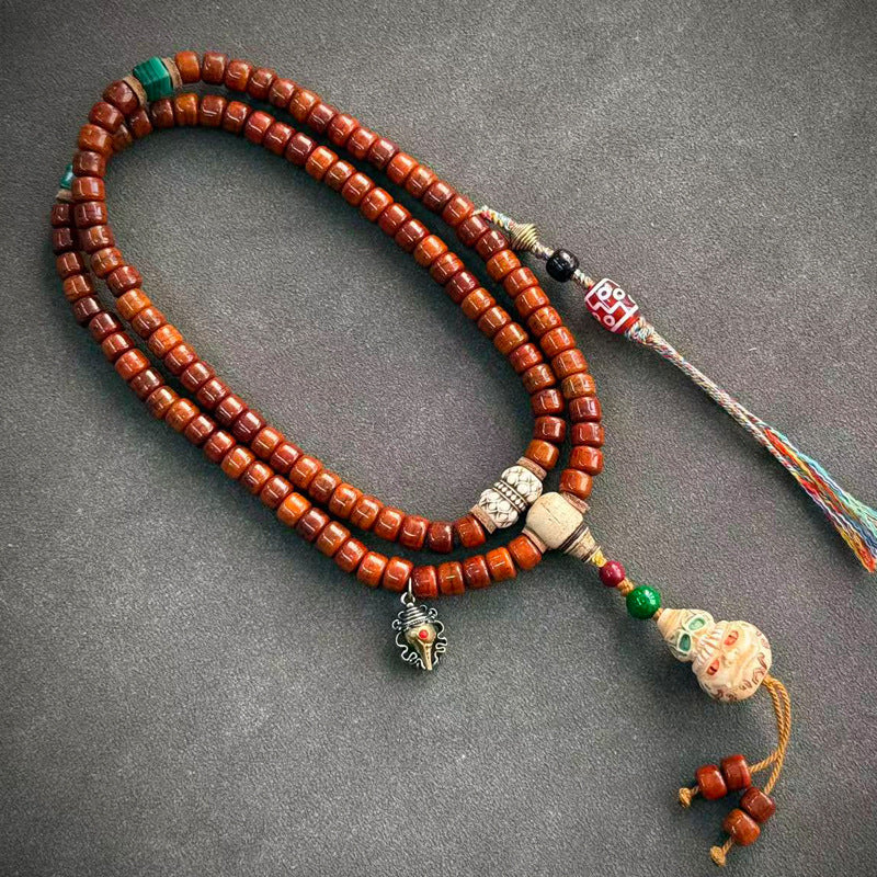 Yak bone mala on grey surface with silver lion guru bead, turquoise nugget and green tassel