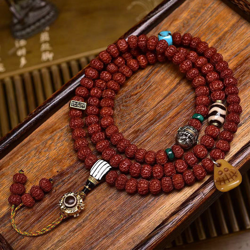 Close-up of rudraksha mala with dzi stone, turquoise and carved bone pendant