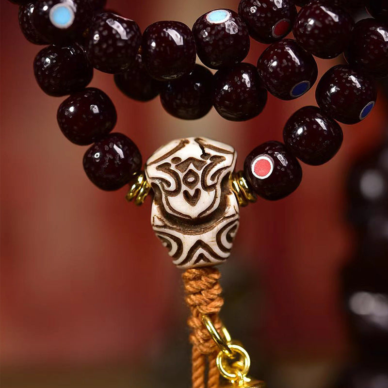 Close-up of carved bone guru bead with Tibetan script and gold ring on cinnabar bodhi mala
