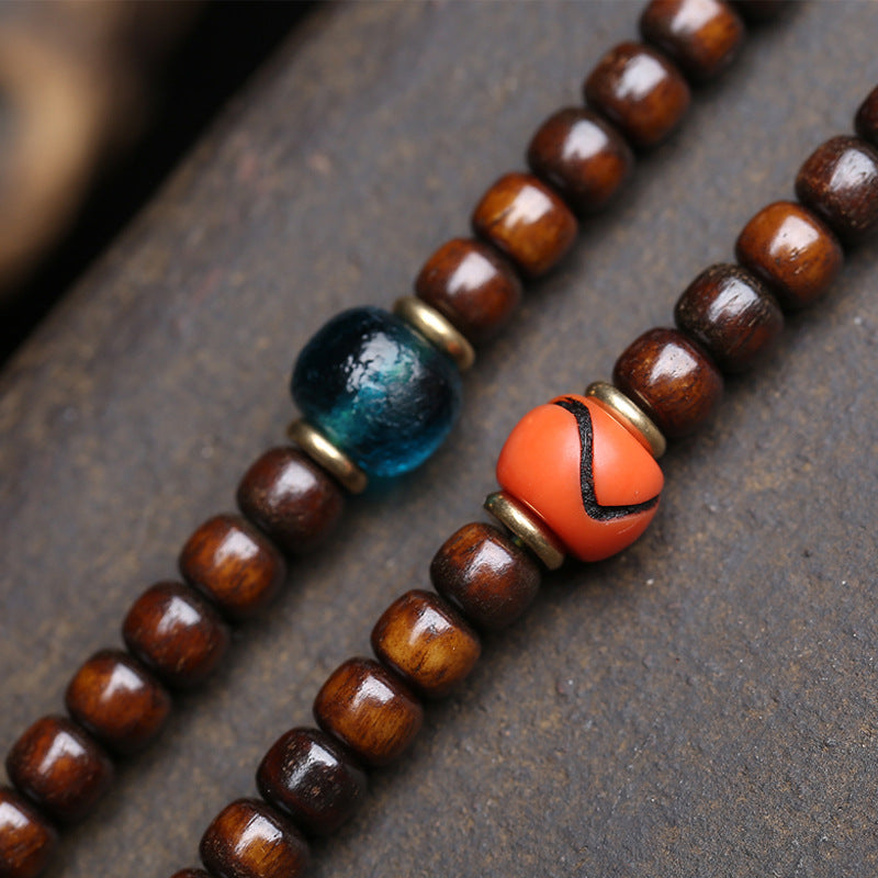 Macro close-up of teal antique glass bead and orange-red dzi accent bead flanked by brass spacers on aged brown barrel bead strand
