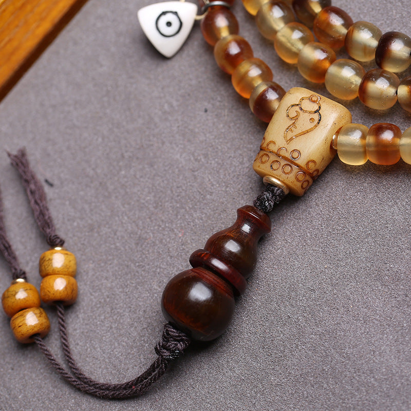 Close-up of carved bone guru bead and ox horn gourd pendant with linen tassels