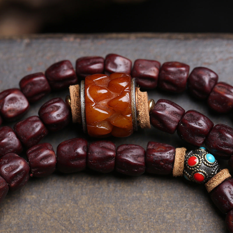 Detail of amber carved spacer bead and silver inlaid metal bead on red sandalwood mala