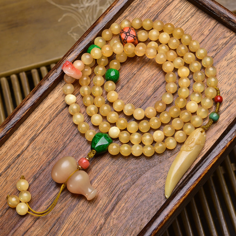 Antler mala on wooden tray showing green jade beads, pink lotus charm and carved bone tooth pendant