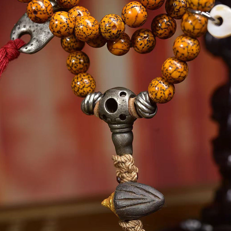 Close-up of silver skull guru bead and rope knot with dark carved pendant on cracked bodhi mala
