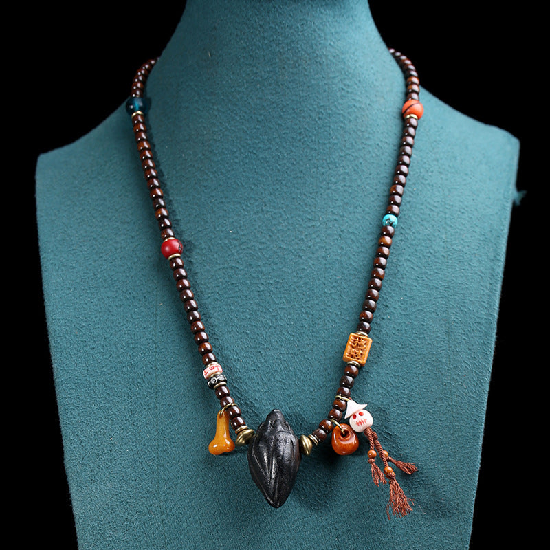 Tibetan mala necklace styled on blue mannequin bust showing full length sweater chain with Tsa Tsa pendant and colorful accent beads against black background