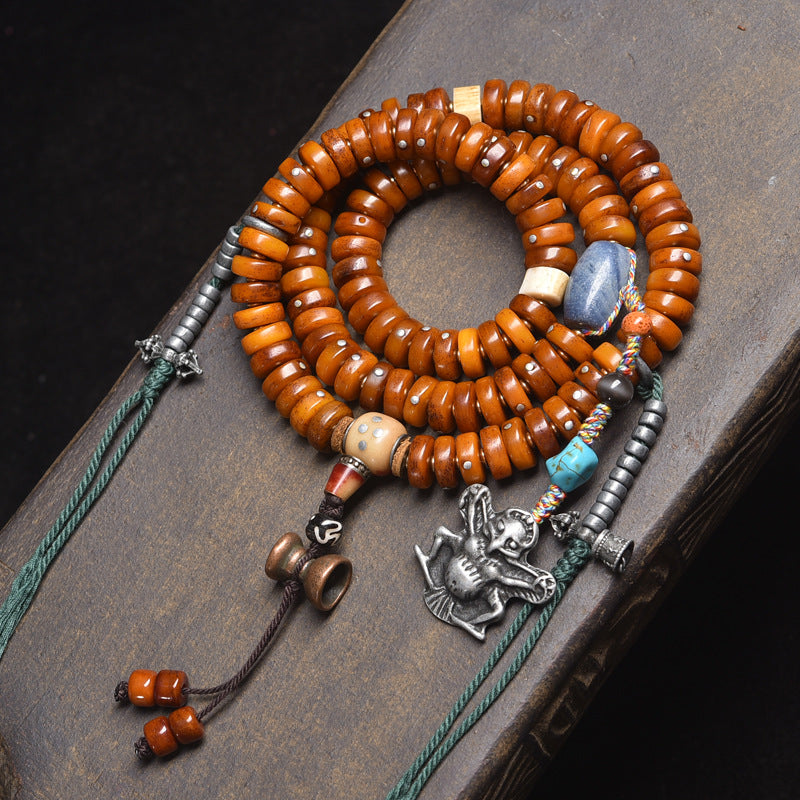 Recycled bone disc 108 mala coiled on dark book with silver Garuda pendant, turquoise bead and colorful tassel