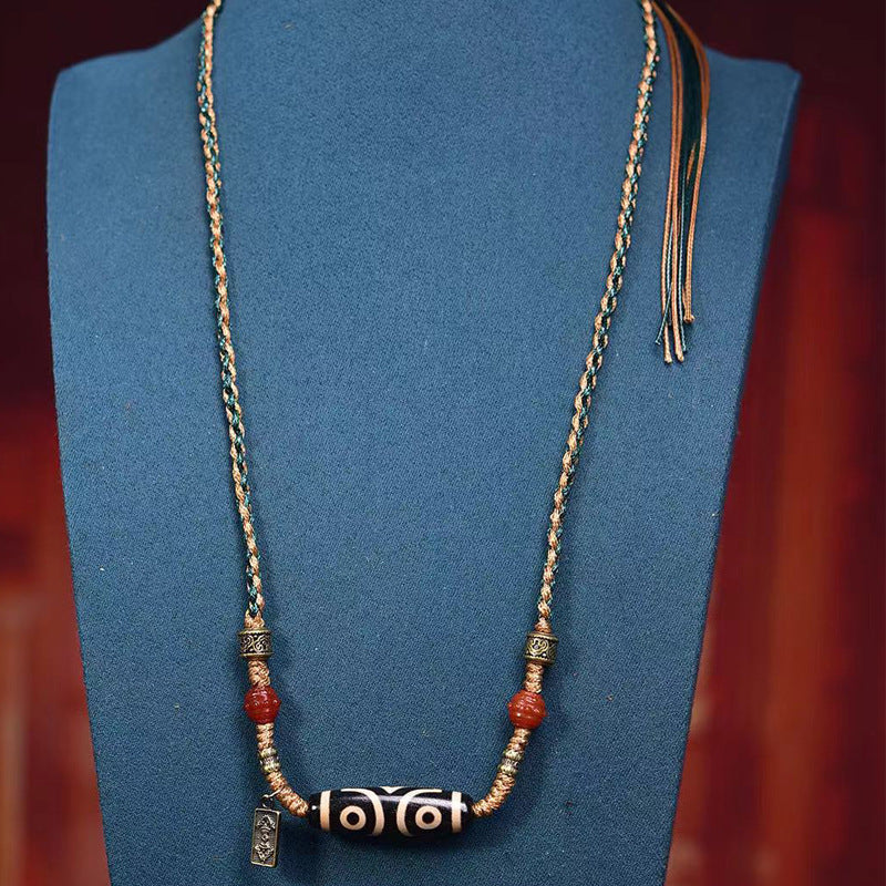 Tibetan three-eye dzi bead necklace styled on blue mannequin bust showing full adjustable length with sliding tassel closure