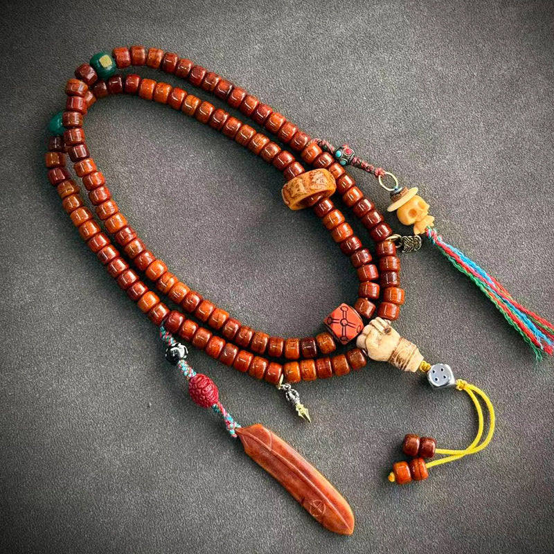 Yak bone mala on grey surface with silver dragon guru bead, turquoise bead and pink tassel