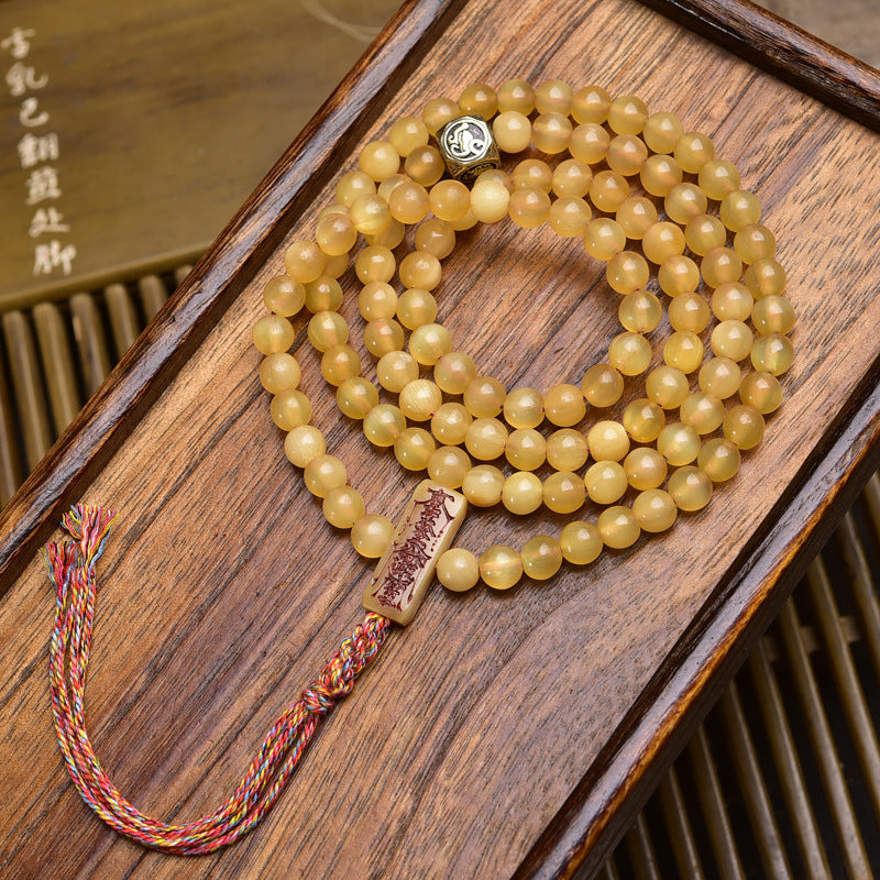 Antler mala coiled on wooden tray with silver yin-yang guru bead and carved bone scripture pendant with colorful tassel