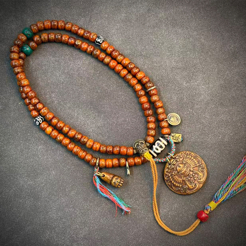 Yak bone mala on grey surface showing bone carved pendant, agate spacer and colorful tassel detail