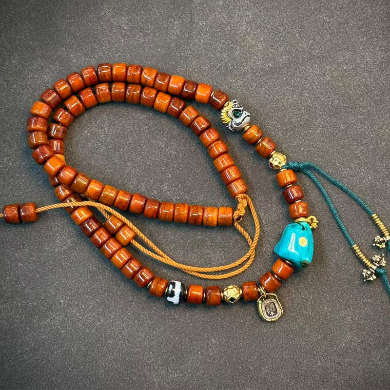 Yak bone mala on grey surface with silver eye charm, turquoise bead and red tassel